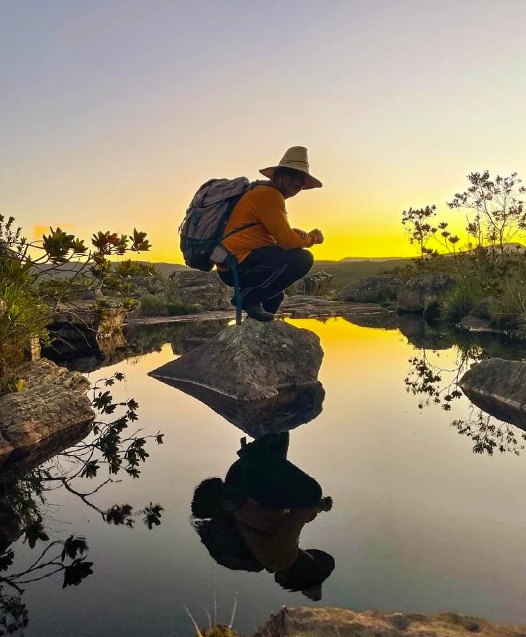 Ney agachado sobre uma pedra no espelho d'água ao pôr do sol